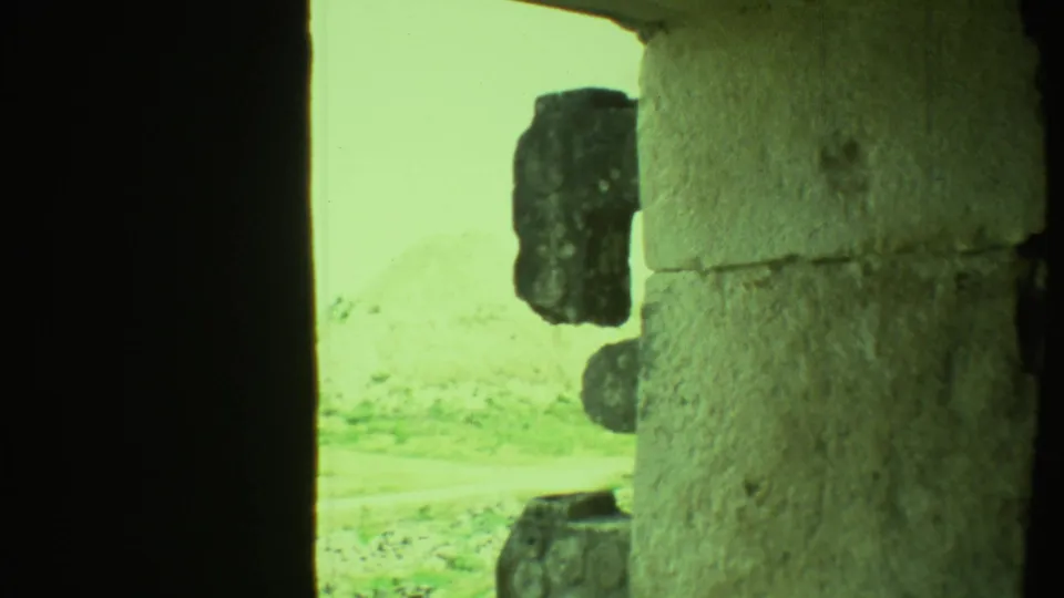 1973 Yucatan 8mm frame looking through a shadowed stone opening toward weathered masonry and pale outdoor ground.