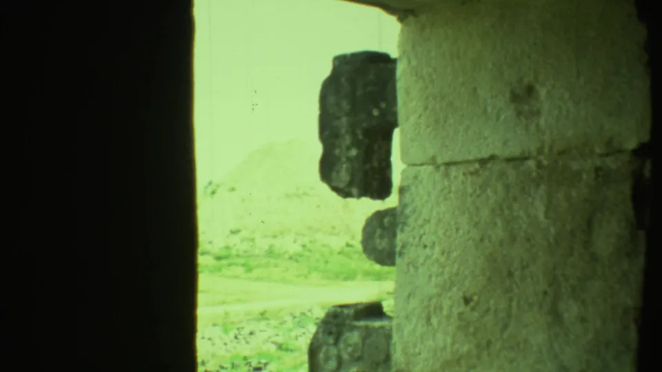 A green-tinted 8mm view from inside or near a stone opening at a Yucatan archaeological site, showing rough blocks and bright ground.