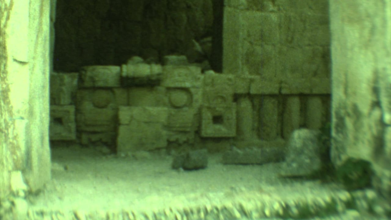 View through stone columns into a dark chamber with carved stone blocks.