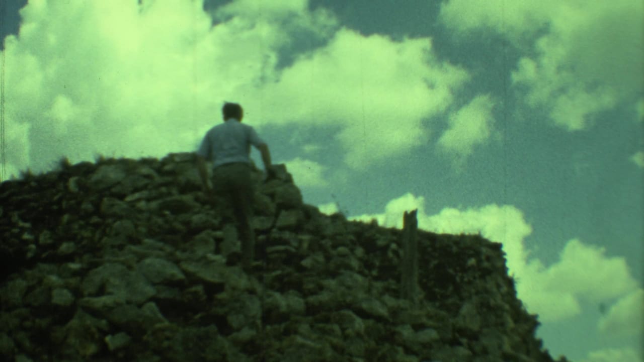 Man ascending a rocky ruin wall with clouds above.