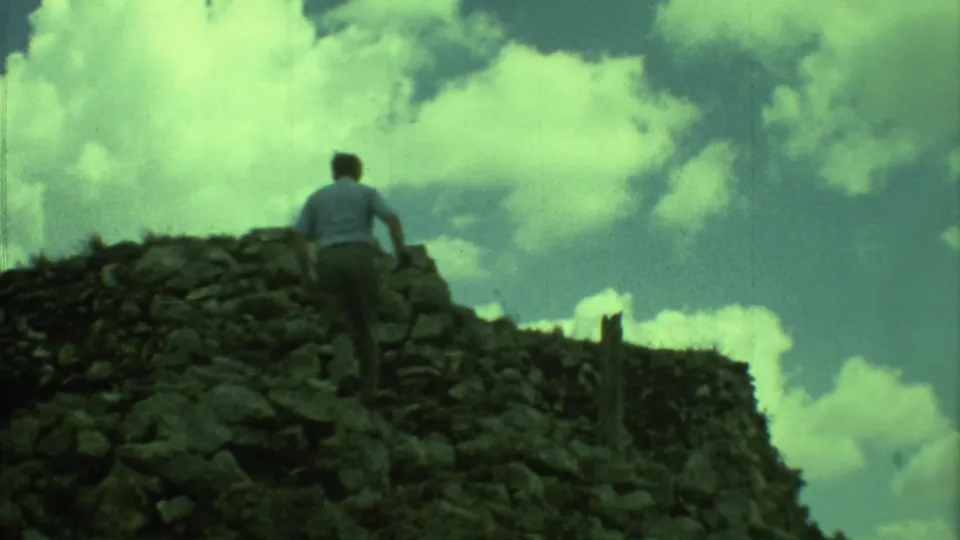 A tourist in a light shirt climbs a rough stone ruin in Yucatan, Mexico, in grainy 1973 8mm footage.