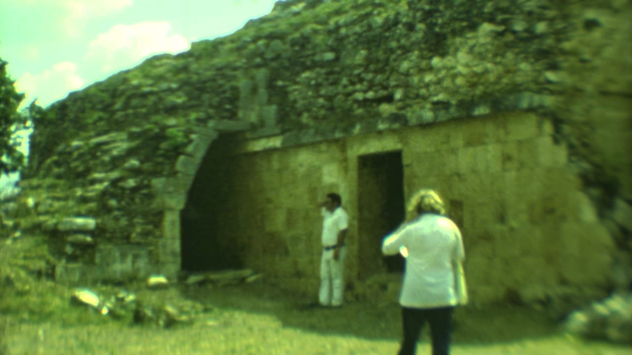 Two adults stand near a dark entrance in a weathered stone structure.