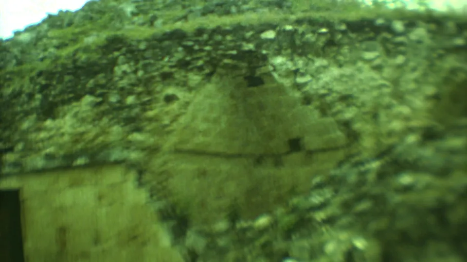 Soft 8mm view of Yucatan stone ruins with rough masonry, vegetation, and part of a dark entrance visible.