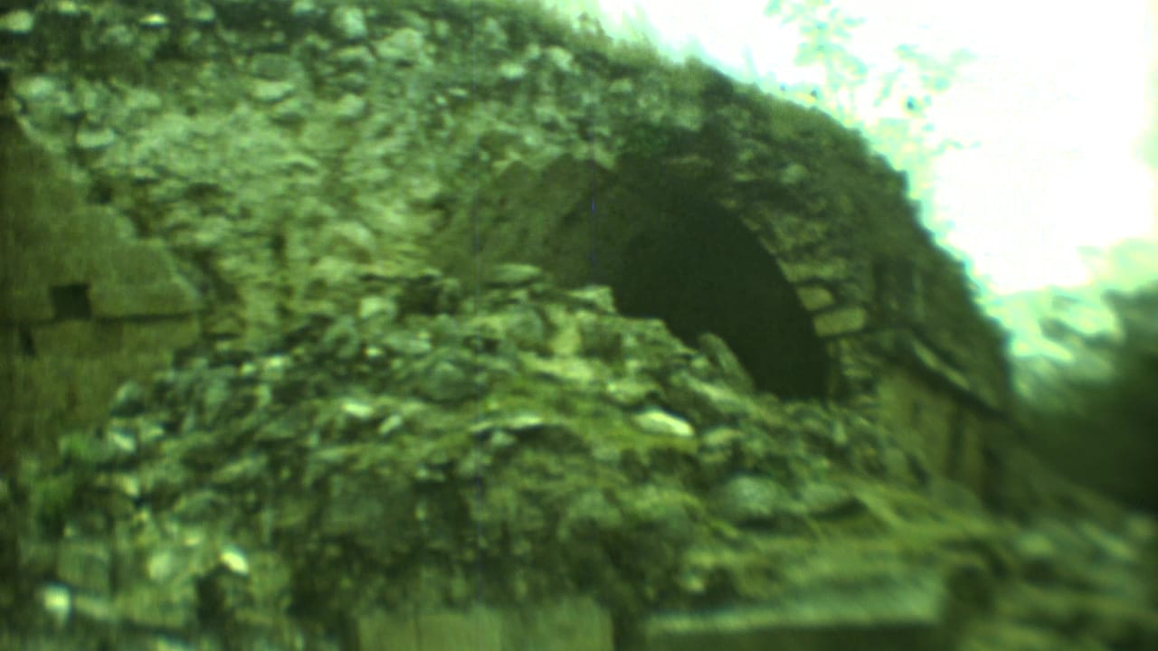 Crumbling stone ruin with a dark arched opening and vegetation above.