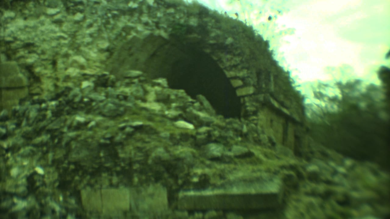 Weathered stone structure with a large arched opening and rubble in front.