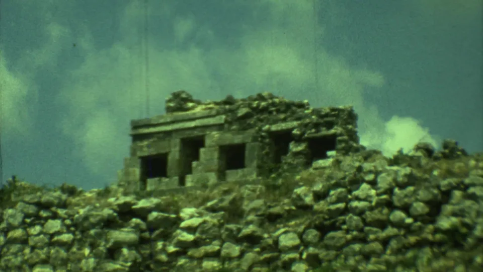 Vintage 8mm frame of the Yucatan ruin, with dark window-like openings and a rough stone foreground.