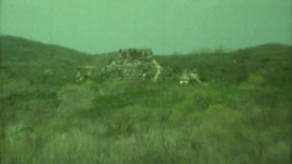 1973 Yucatan frame showing a distant stone ruin or rock structure in scrubland, backed by low hills and soft 8mm texture.