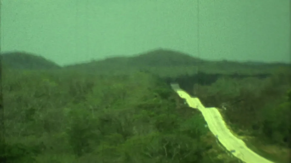 1973 Yucatan travel footage frame showing a pale winding path through brush and low forested hills.