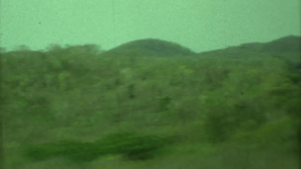 Soft-focus 8mm frame from Yucatan showing green hills, dense brush, and a pale sky during a handheld pan.
