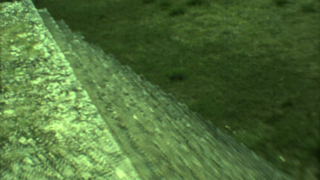 Green-tinted 8mm frame from Yucatan showing a tall stone stair edge and sloped grassy surroundings.