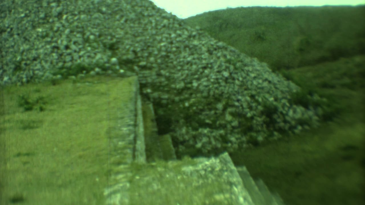 1973 Yucatan 8mm frame showing a weathered stepped stone pyramid rising from grass with lush vegetation in the background.