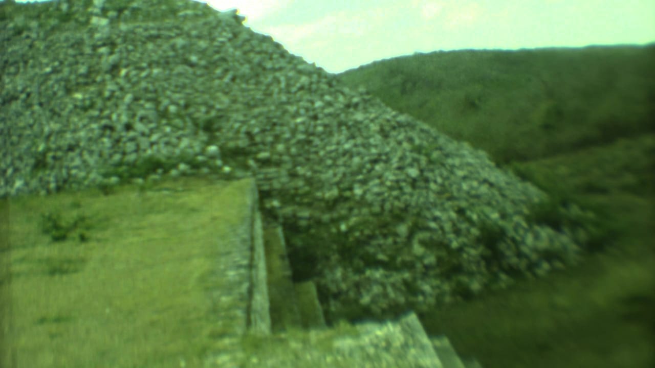 Stone steps leading up toward a large weathered pyramid structure surrounded by greenery.