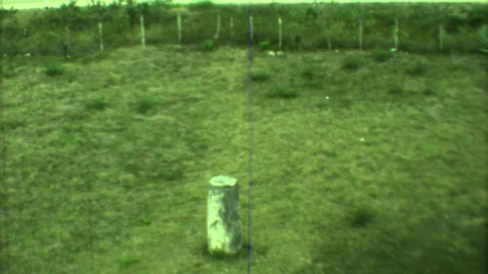1973 Yucatan 8mm frame showing an upright stone marker in a grassy clearing, with a simple fence and trees behind it.
