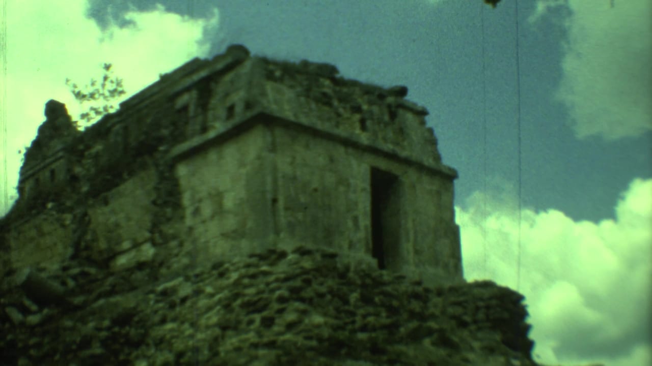Weathered stone ruin with a dark doorway seen from below against a cloudy sky.