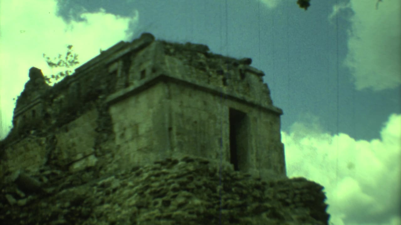 1973 Yucatan 8mm frame with the stone ruin centered, showing a dark opening, eroded masonry, and scattered clouds.