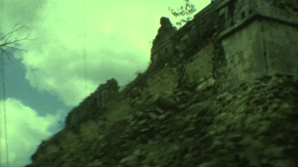 1973 Yucatan 8mm frame looking along eroded stonework toward a Mayan ruin, with clouds and visible film wear.