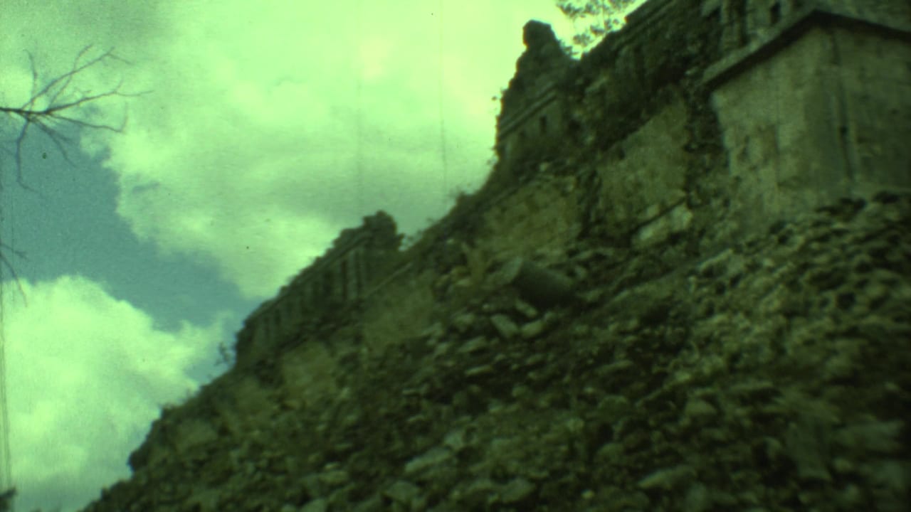 Handheld 8mm view of a weathered Yucatan ruin wall with loose stones and overcast sky.