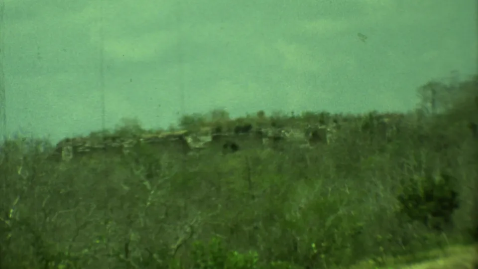 Green-shifted 8mm frame from Yucatan, Mexico, showing trees and a low stone structure near the archaeological grounds.