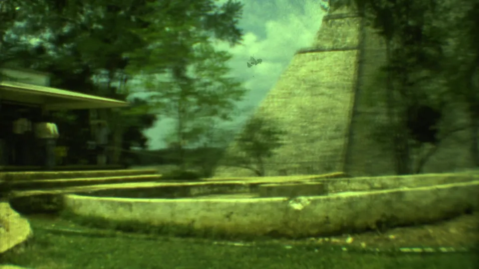 1973 Yucatan home-movie frame showing a pavilion and stone fountain wall near a large pyramid at an archaeological site.