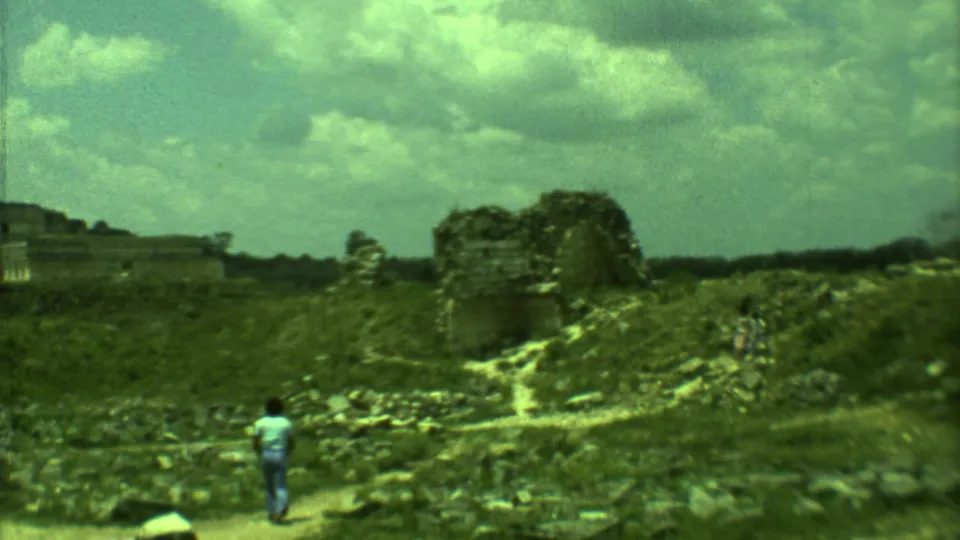 Handheld 8mm view of a tourist walking on a path toward low Mayan ruin structures in Yucatan, Mexico.