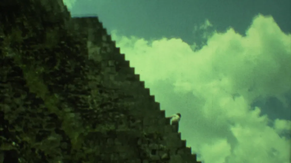 A large Mayan pyramid in Yucatan fills the frame as a distant visitor appears on the steep stone stairs.