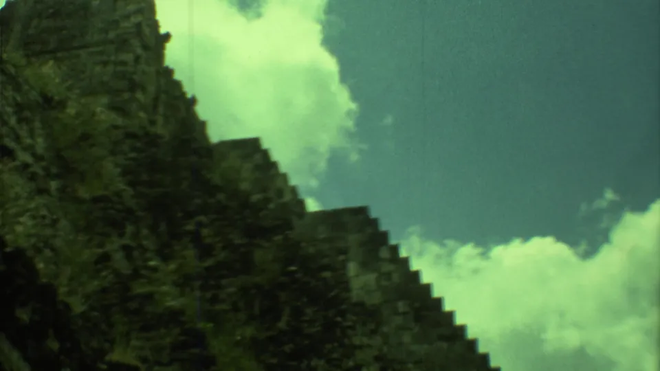 The 1973 home-movie view holds on the weathered Mayan pyramid stones and stepped edge under a bright clouded sky.