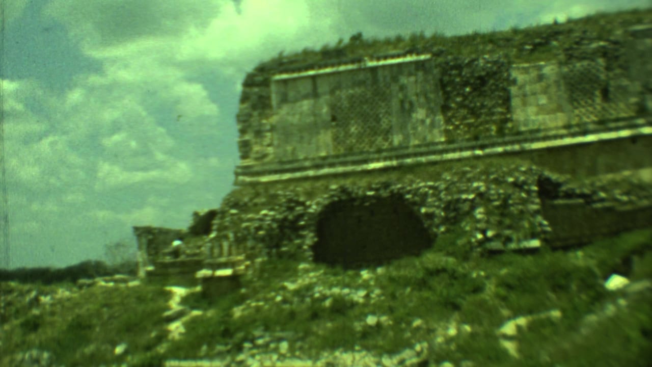 1973 Yucatan frame of a low weathered stone structure with grass, path, and a dark opening.