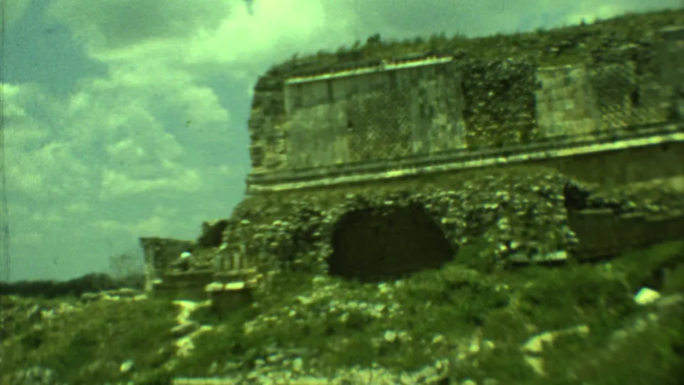 1973 Yucatan frame of a low weathered stone structure with grass, path, and a dark opening.