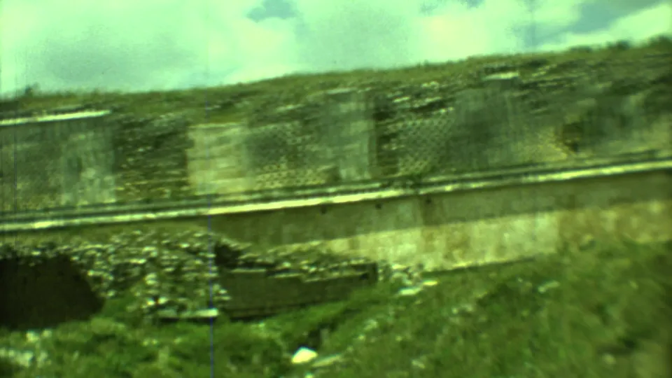 1973 Yucatan frame with a closer view of rough stone masonry, grass, and cloudy sky during a handheld pan.