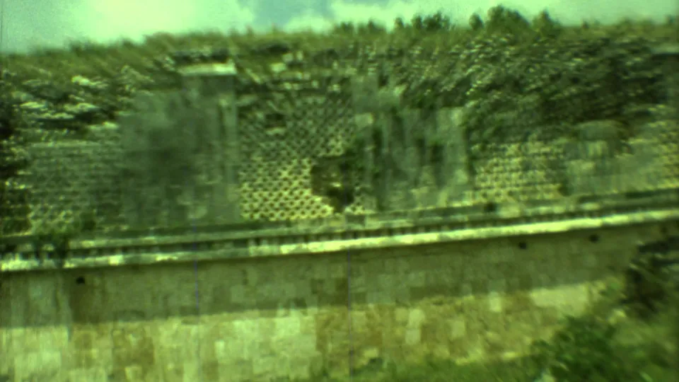 1973 Yucatan home-movie frame showing a closer, blurred view of lattice-like stonework and a weathered ruin wall.