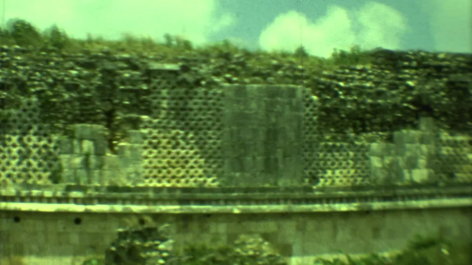 1973 Yucatan home-movie frame of Mayan stone ruins, with patterned masonry, broken upper walls, and soft green film tint.