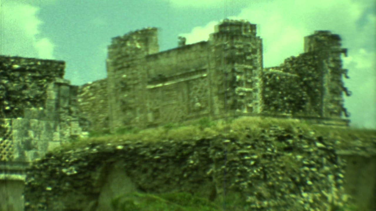 Weathered stone ruin wall with vegetation below and bright clouds above.