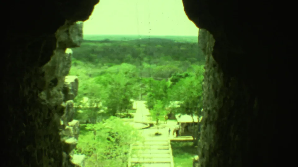 1973 Yucatan 8mm frame looking through a dark stone opening toward a path, greenery, and small distant visitors.