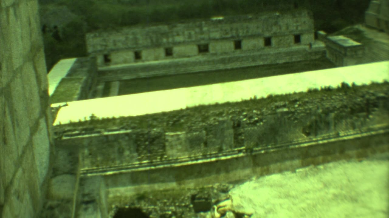 1973 8mm view over Mayan stone structures in Yucatan, with a pale courtyard and surrounding greenery.