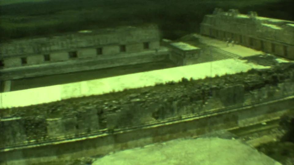 Vintage 8mm frame of Mayan ruins in Yucatan, with a broad pale courtyard and distant masonry structure.
