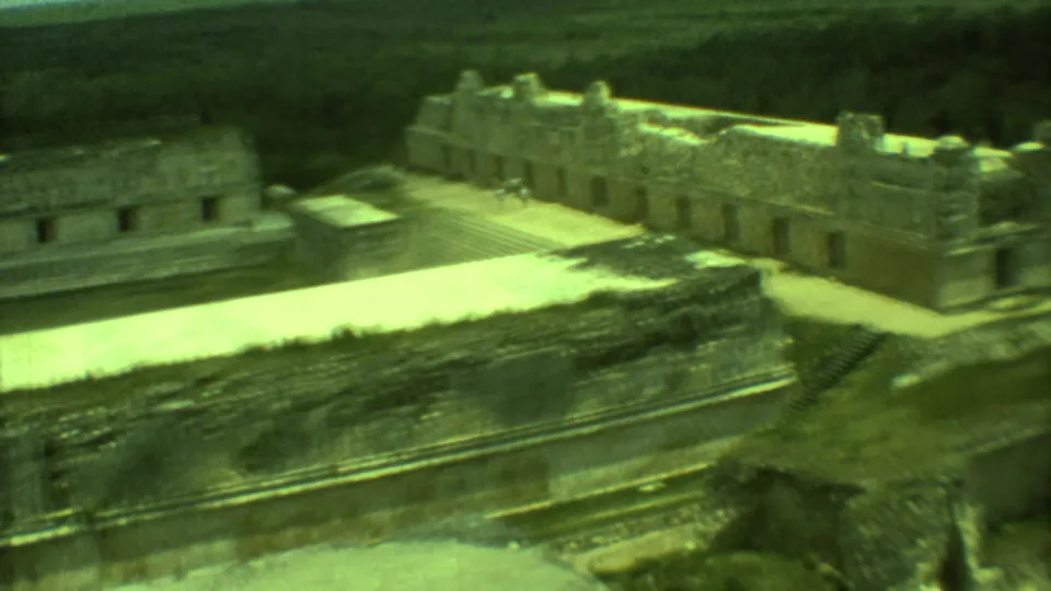 1973 Yucatan home-movie frame showing stepped stone architecture, open paving, and possible tiny distant visitors.