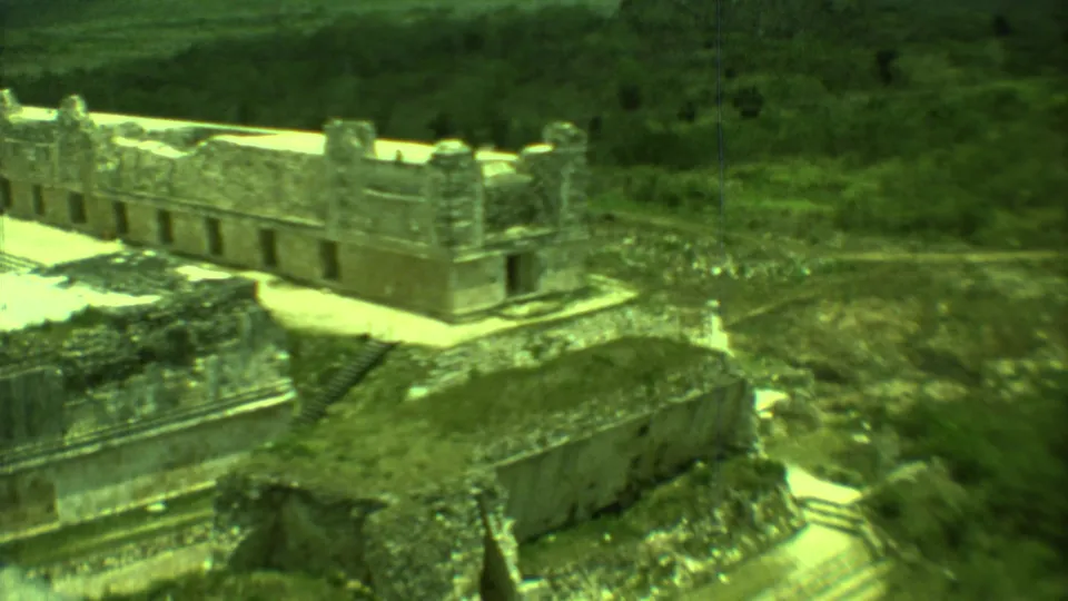 Vintage 8mm Yucatan view of Mayan ruins with stone walls, stepped edges, and scrub vegetation in frame.