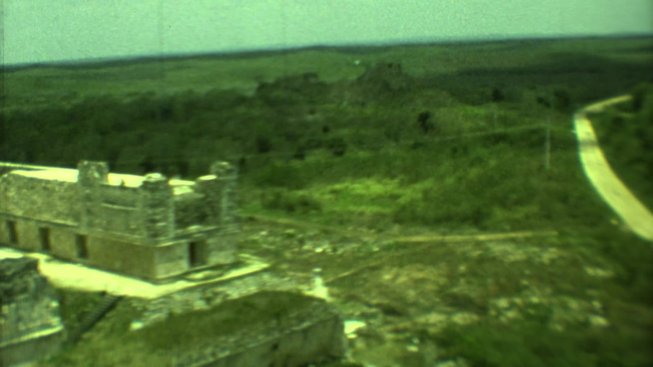 Distant stone ruin beside greenery with a pale road curving through the landscape.