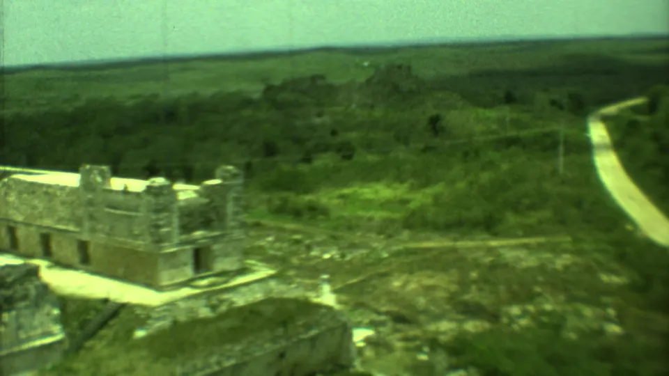 1973 Yucatan 8mm frame showing a distant stone ruin, surrounding green terrain, and a light road crossing the landscape.
