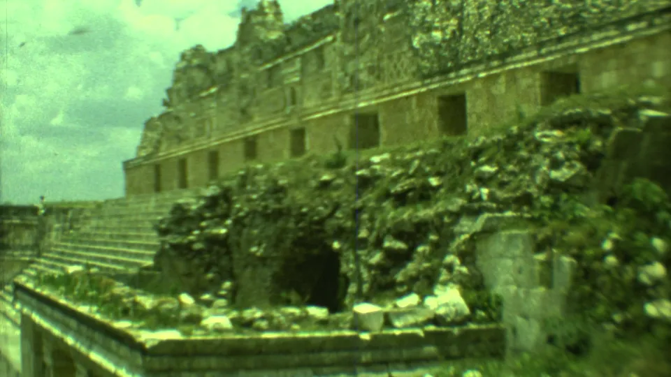 1973 Yucatan travel footage frame showing a weathered stone facade beside stairs and plant-covered rubble.