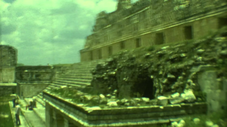 1973 Yucatan home-movie frame with distant tourists near broad stone steps and a weathered ruin facade.