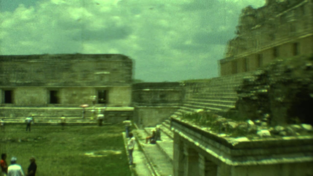 Green-tinted 8mm frame of tourists crossing an open courtyard beside ancient stone architecture in Yucatan, Mexico.