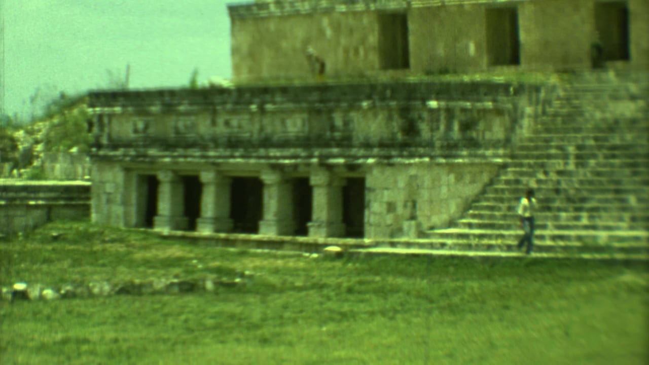 1973 8mm view in Yucatan, Mexico, showing a colonnaded stone ruin, broad steps, grass, and a distant visitor for scale.
