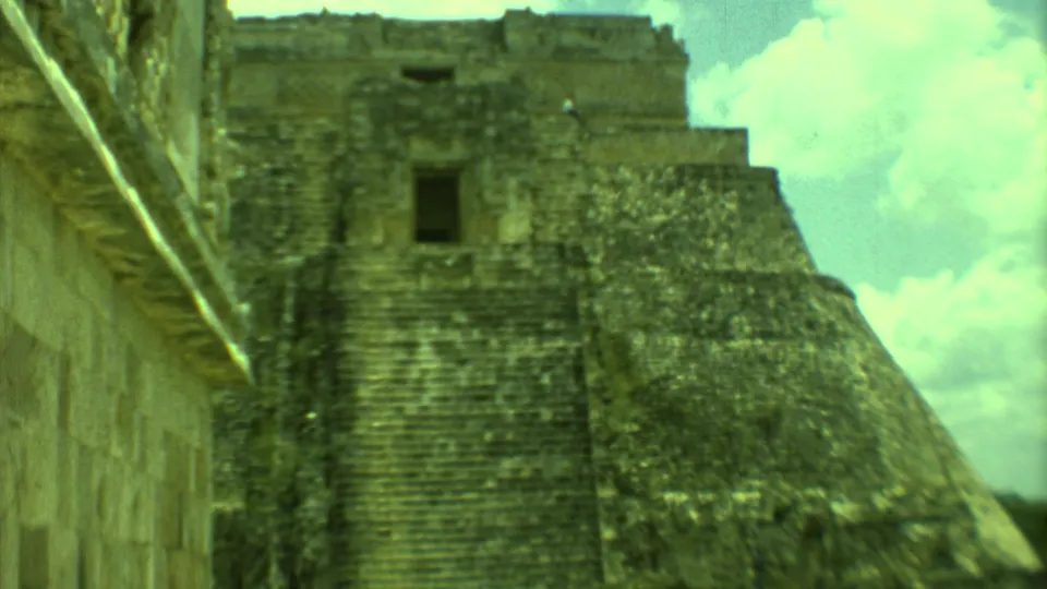1973 8mm Yucatan footage showing a weathered Mayan stepped pyramid, adjoining wall, dark opening, and bright sky.