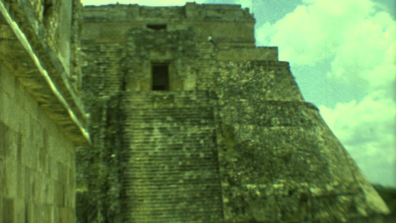 Stone pyramid with steep steps beside a masonry wall under bright clouds.