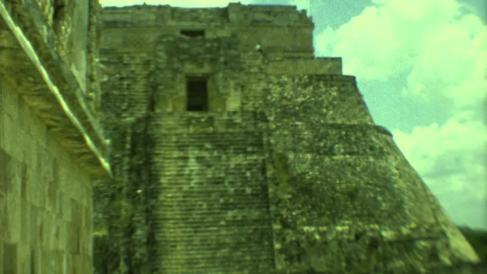 1973 Yucatan 8mm frame showing a weathered stone pyramid and nearby wall under a bright, clouded sky.