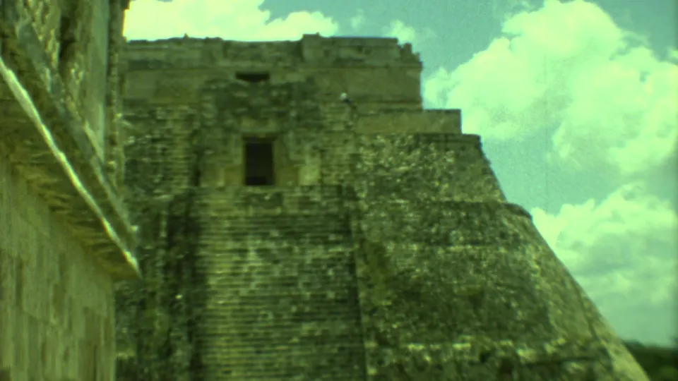 1973 Yucatan travel footage frame with a close view of the pyramid face, upper platform, and bright clouds.