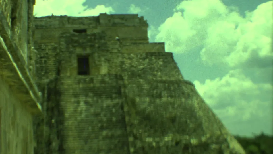Soft 8mm frame from Yucatan showing the upper stone pyramid, dark doorway-like opening, and bright clouds.