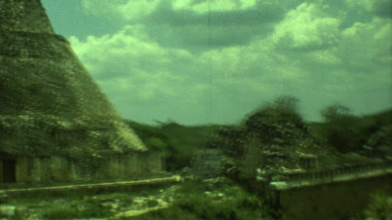1973 8mm view of Mayan ruins in Yucatan, showing a stone structure, pointed roof form, vegetation, and cloud cover.