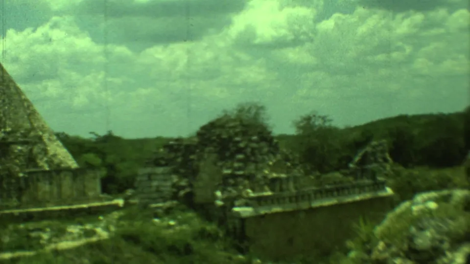 1973 Yucatan home-movie frame showing Mayan stone structures, broken masonry, low barriers, and surrounding vegetation.